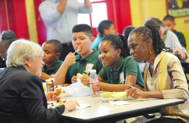 Source: Getty Images. New York City Schools Chancellor Carmen Fariña (Left) and Mayor de Blasio’s wife, Chirlane McCray (Right) eat lunch with students at Journey Prep School in the Bronx where many students depend on free lunch. 